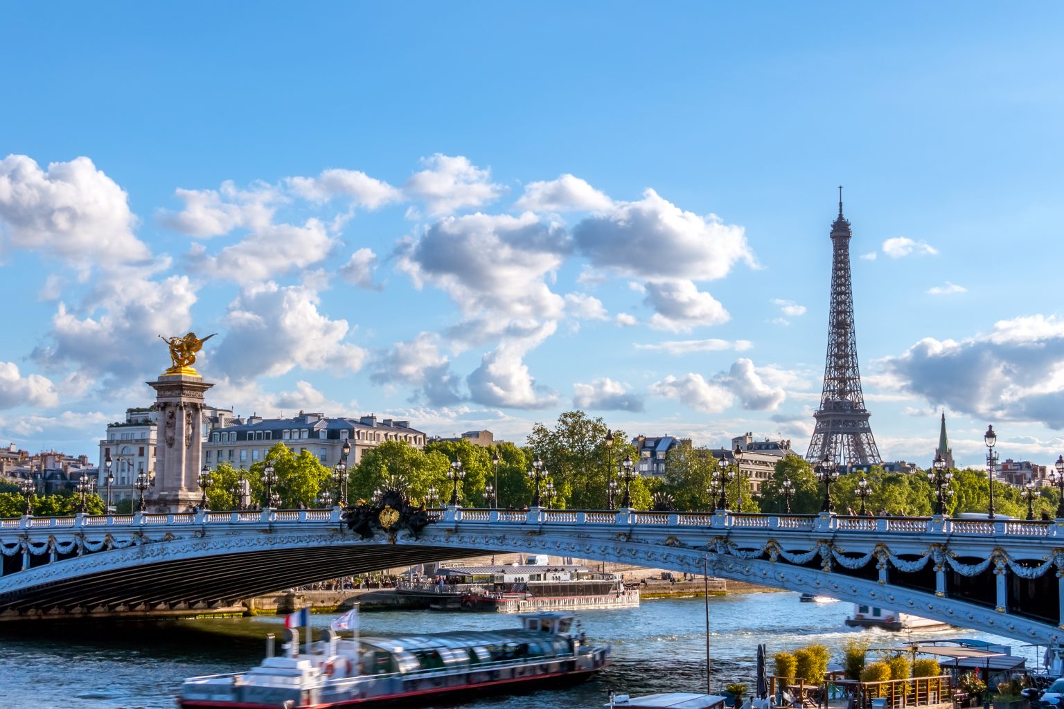 France. Sunny summer day in Paris. Pleasure boat under the bridge of Alexander III over the river Seine. Eiffel Tower